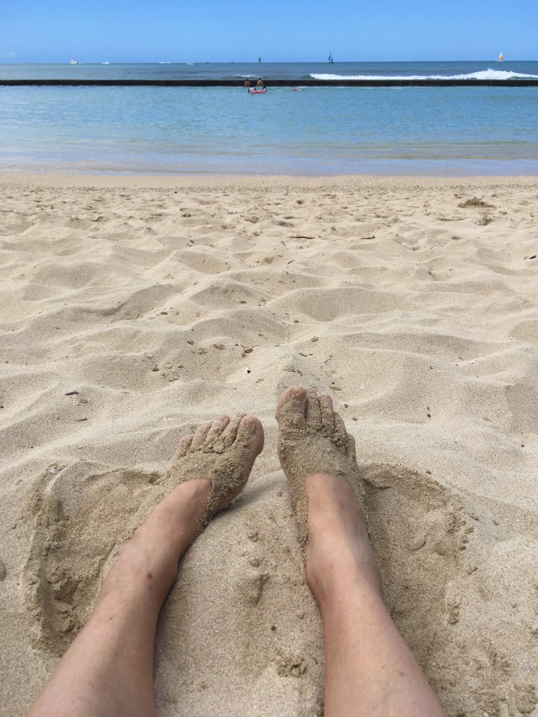 someone sitting on a beach with her feet in the sand. 